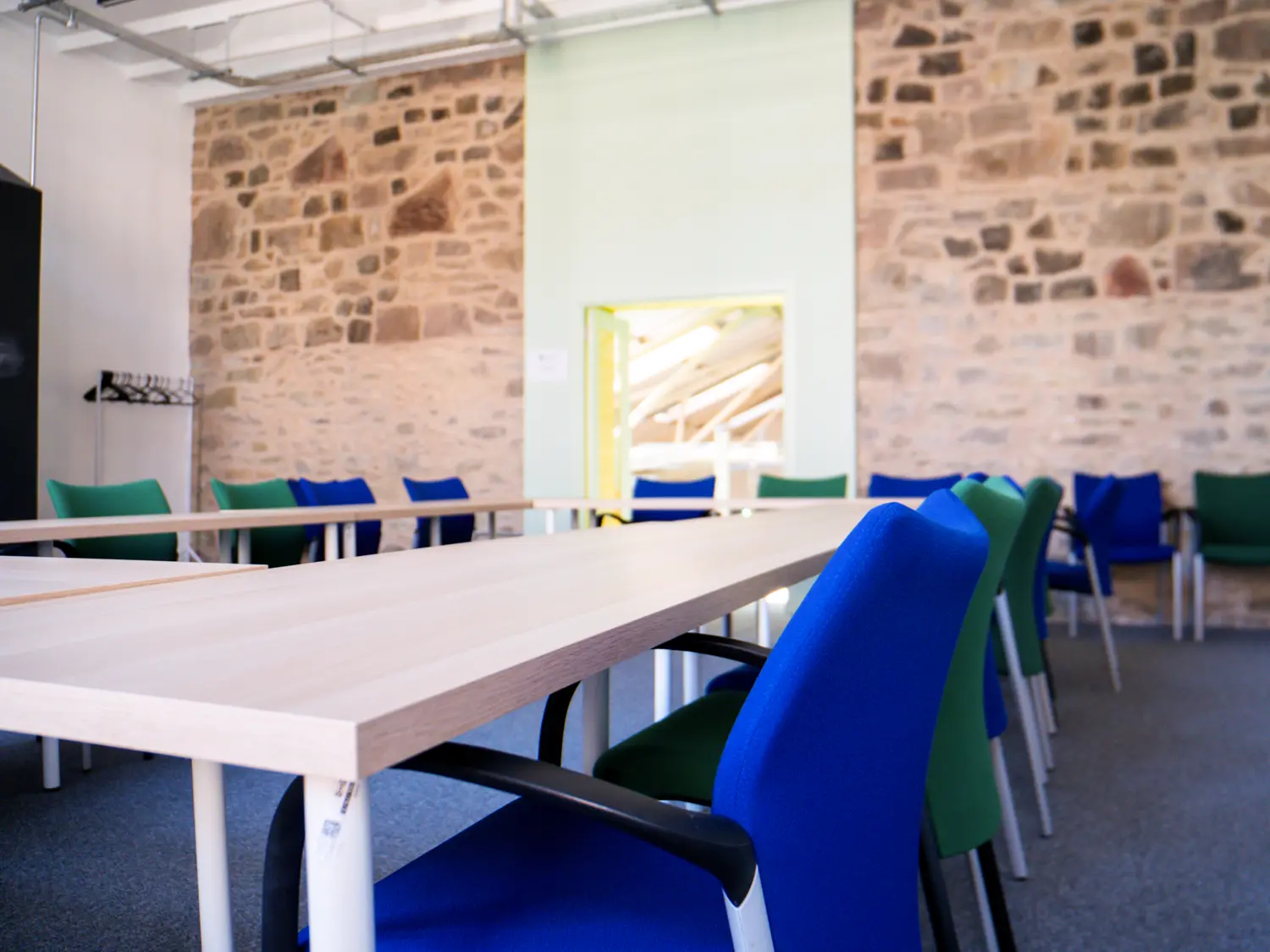 Photo of the granary space showing original stone walls in the background and a large table with blue chairs in the foreground.