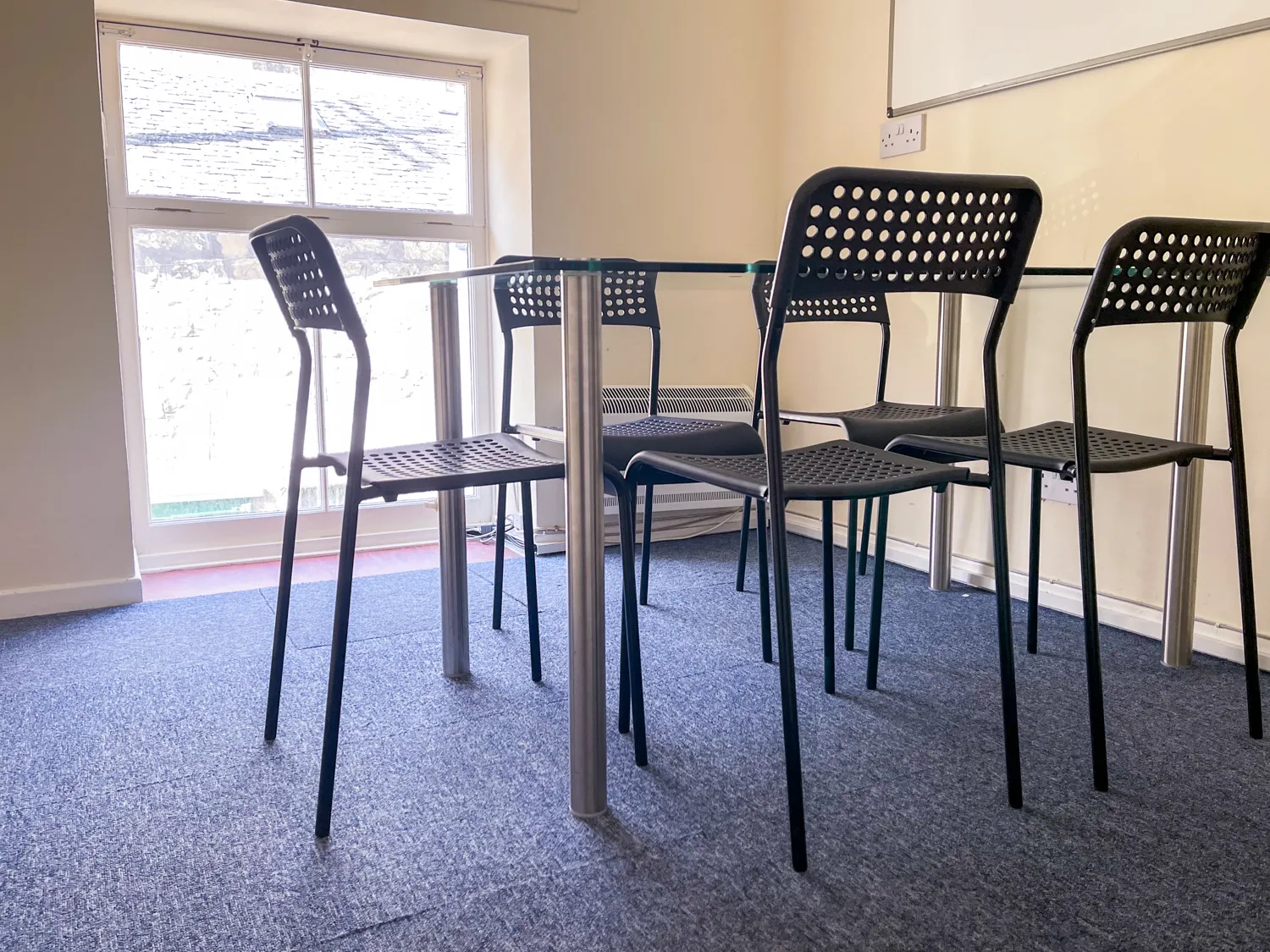 Photo showing a meeting room with a large window and a glass table and chairs on blue carpet tiles