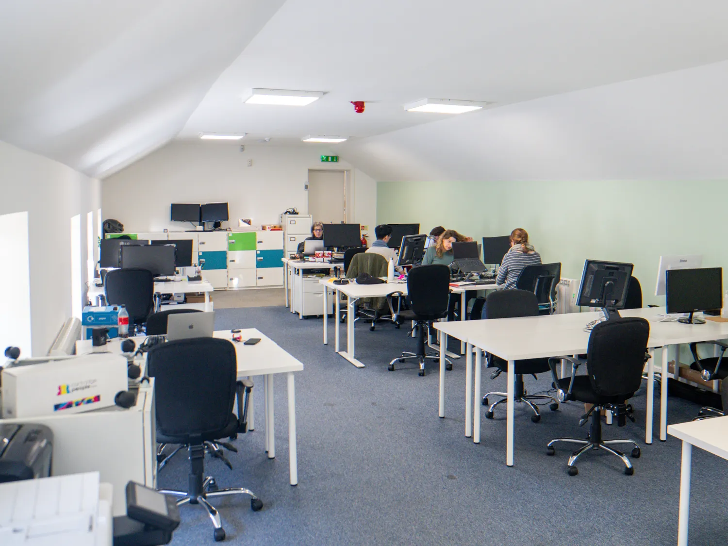 Large white and pale green office space with desks on a grey carpet.