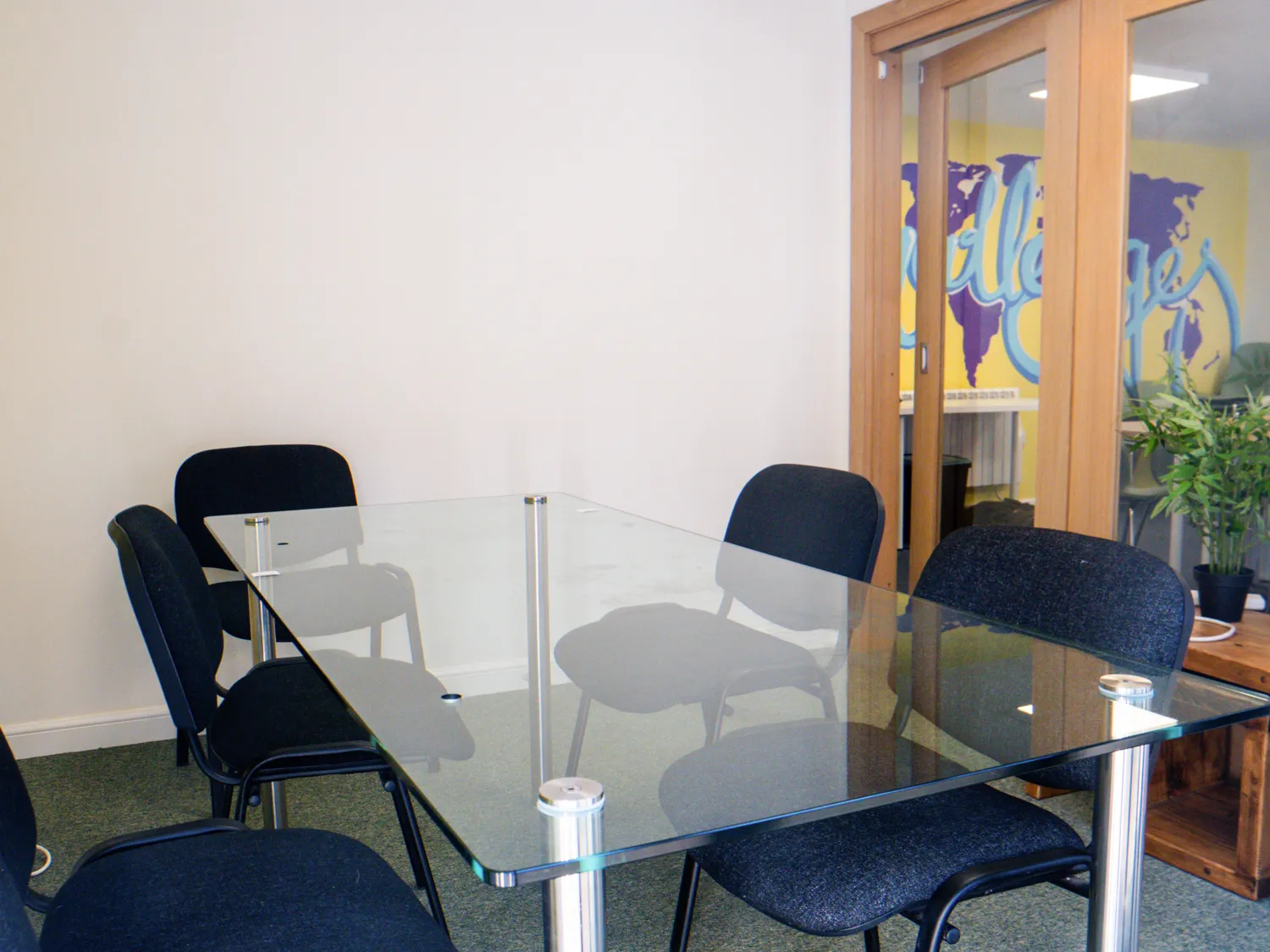 Photo of a meeting room with a glass table and chairs. In the background are glass panels looking through into another space.